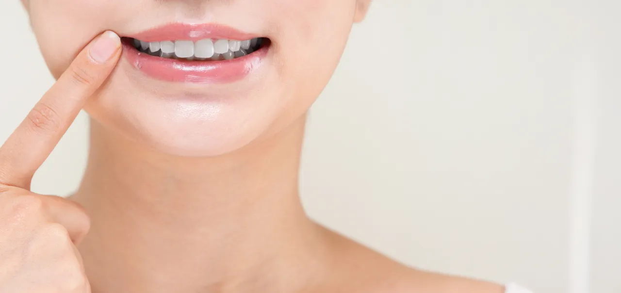 口元を指さして歯を見せる女性の笑顔